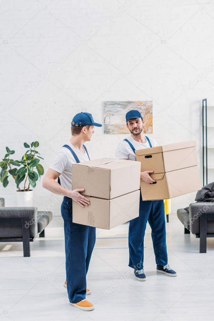 two movers in uniform carrying cardboard boxes in apartment with copy space