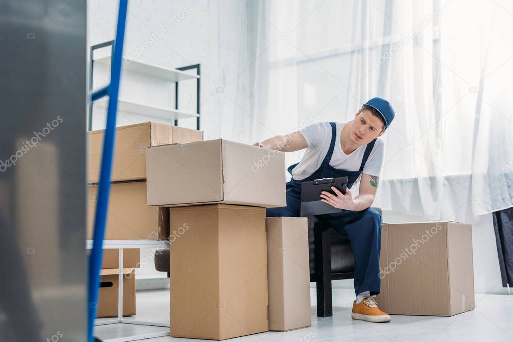 mover sitting near cardboard boxes and holding clipboard in apartment