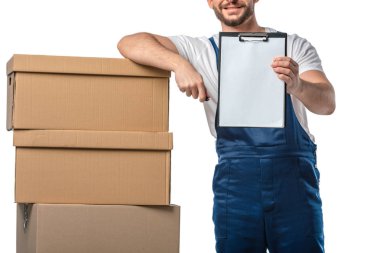 cropped view of mover in uniform holding blank clipboard near cardboard boxes isolated on white clipart
