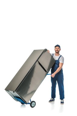 yakışıklı Mover memur kamera bakıyor ve el kamyonunda buzdolabı taşıma kopya alanı ile beyaz izole