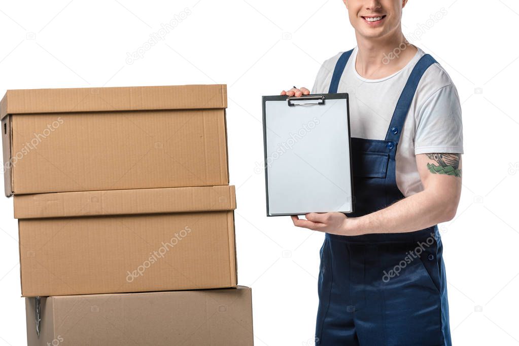 cropped view of mover in uniform holding blank clipboard near cardboard boxes isolated on white