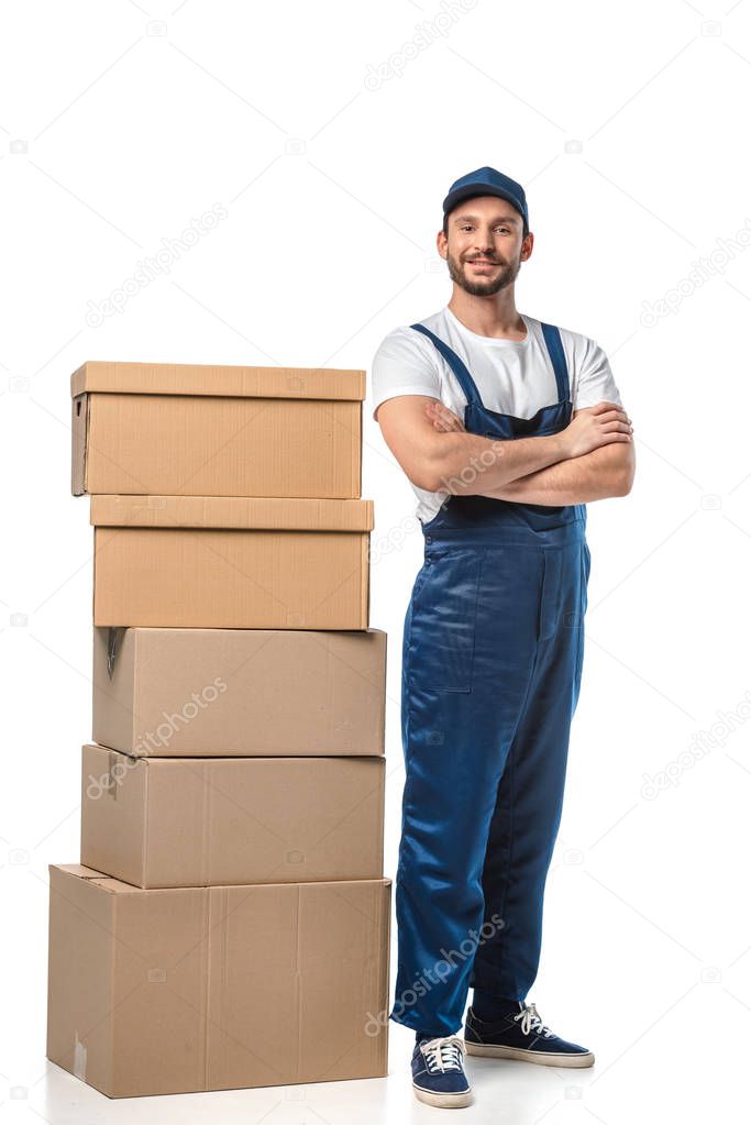 handsome mover in uniform with cardboard boxes looking at camera and smiling isolated on white