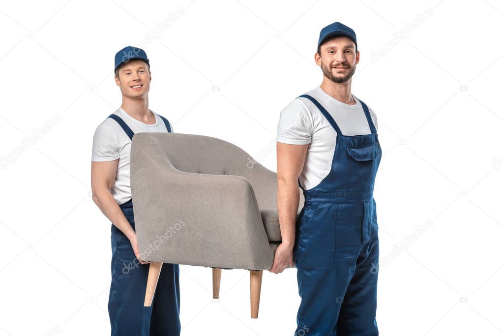two movers looking at camera and transporting grey armchair isolated on white