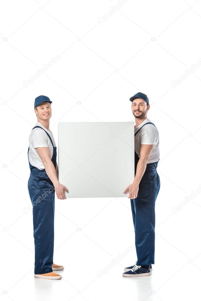 two smiling movers looking at camera while holding blank box isolated on white