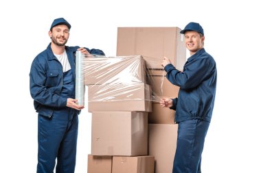 iki Movers kamera bakıyor ve streç film rulo ile karton kutular sarma beyaz izole 