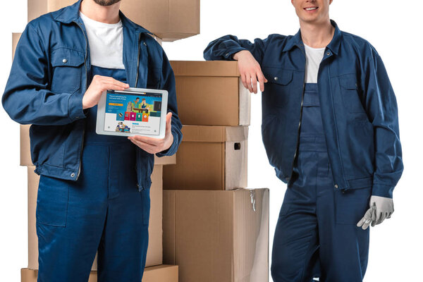 cropped view of two movers with cardboard boxes presenting digital tablet with amazon app on screen isolated on white