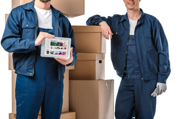 cropped view of two movers with cardboard boxes presenting digital tablet with aliexpress app on screen isolated on white
