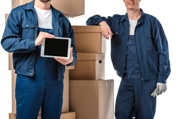 cropped view of two movers with cardboard boxes presenting digital tablet with blank screen isolated on white