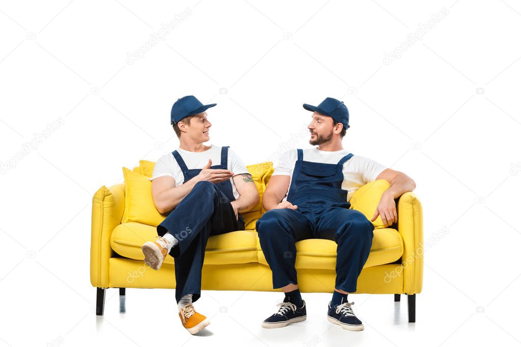 two movers in uniform sitting on yellow sofa and looking at each other on white