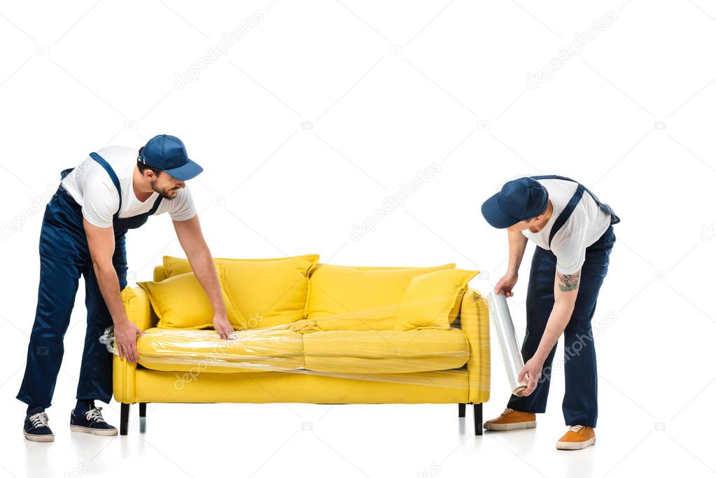 two movers wrapping yellow sofa with roll of stretch film on white