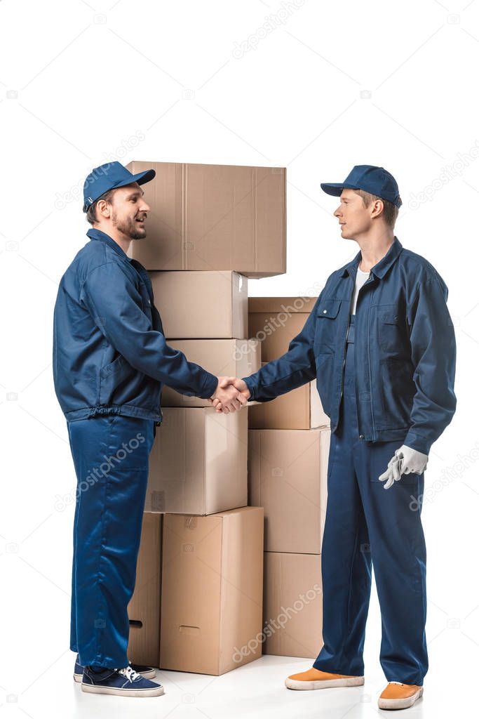 two movers in uniform looking at each other and shaking hands near cardboard boxes on white