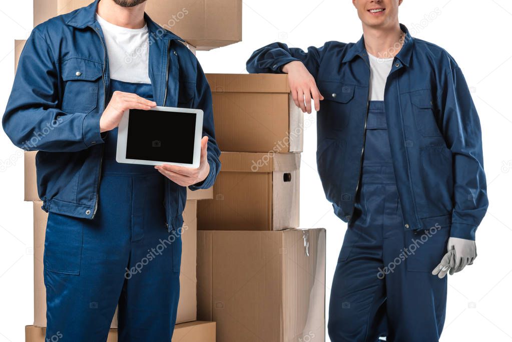 cropped view of two movers with cardboard boxes presenting digital tablet with blank screen isolated on white
