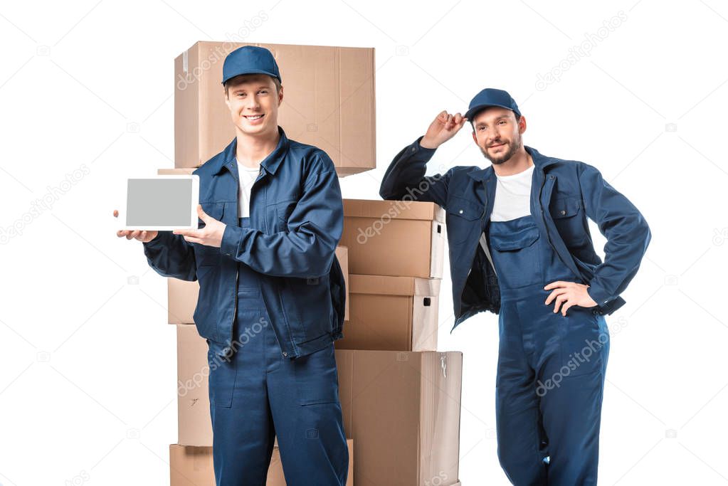 two movers with cardboard boxes looking at camera and presenting digital tablet with blank screen isolated on white