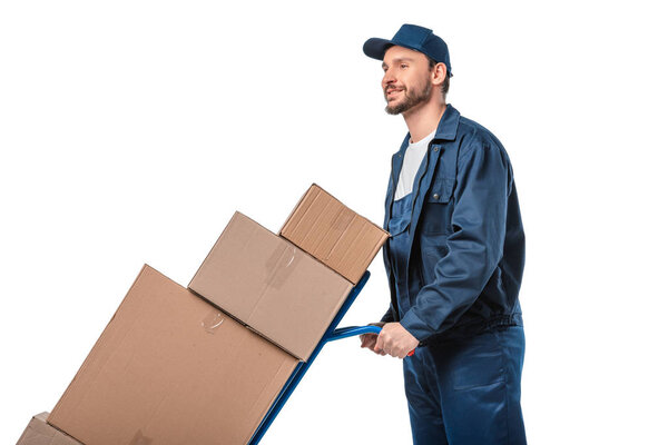 handsome mover in uniform transporting cardboard boxes on hand truck isolated on white with copy space