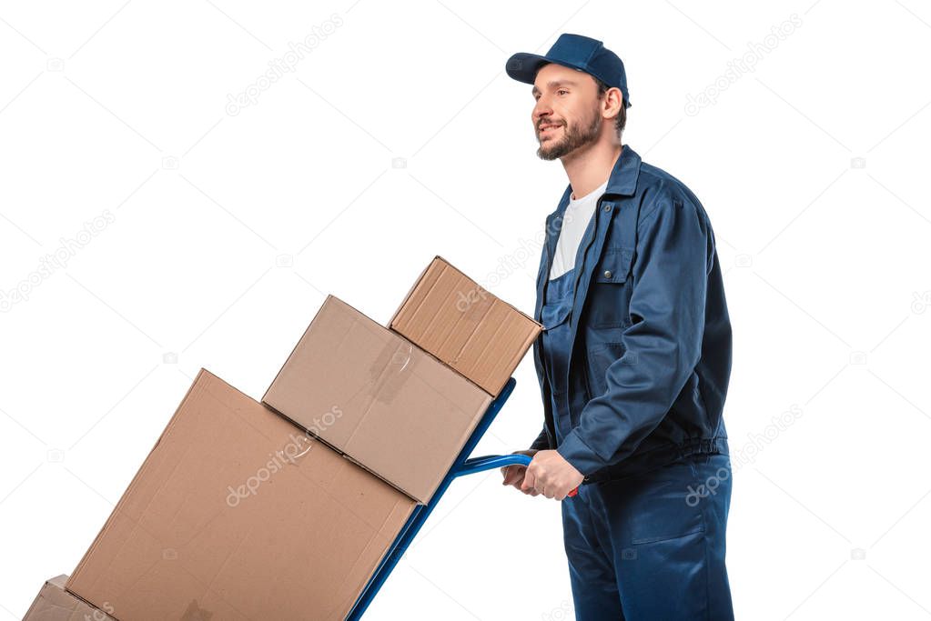 handsome mover in uniform transporting cardboard boxes on hand truck isolated on white with copy space