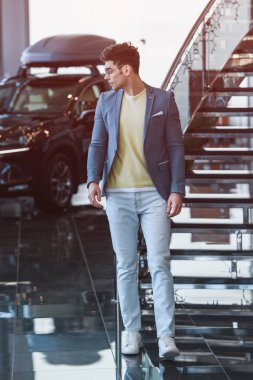 handsome stylish man in glasses standing in car showroom  clipart