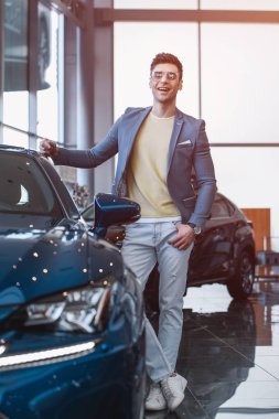 Araba showroom kesişmiş bacaklar ile otomobil yakınında ayakta gözlük çetin adamın seçici odak 