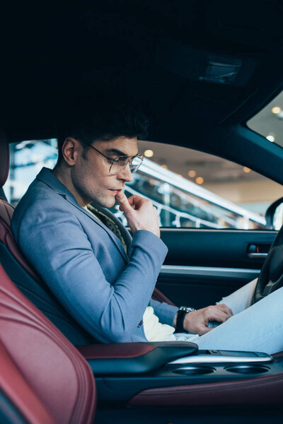 pensive man in glasses thinking while sitting in automobile 