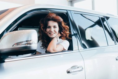 selective focus of cheerful curly woman smiling while sitting in automobile  clipart