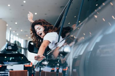 selective focus of excited curly woman screaming while sitting in automobile  clipart