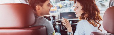 panoramic shot of happy woman and handsome man looking at each other while sitting in automobile  clipart