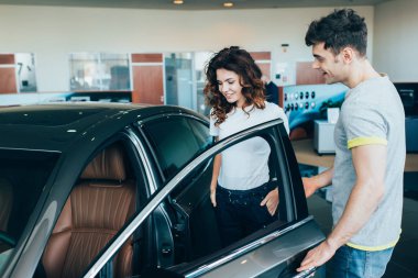 selective focus of handsome man standing near attractive woman while opening car door  clipart
