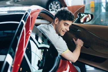 selective focus of handsome man sitting in new red car in car showroom clipart
