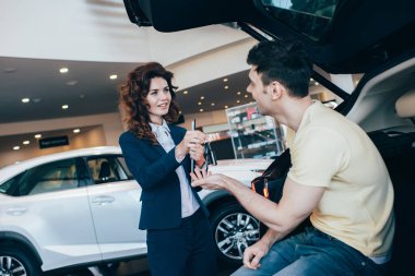 selective focus of happy customer taking car keys from attractive car dealer clipart