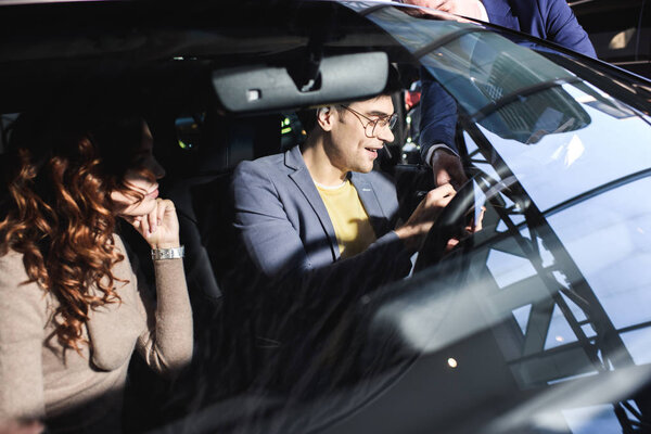 cropped view of car dealer standing near cheerful man and curly woman in car 