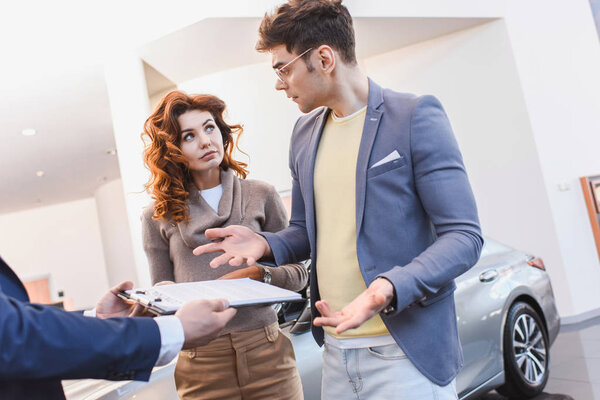 cropped view of dealer holding clipboard with contract near stylish man and curly attractive woman 