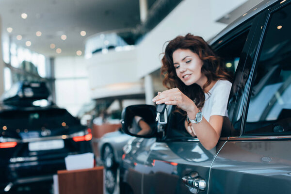 селективный фокус кудряшки, держащей ключи, глядя в окно в автомобиле
 