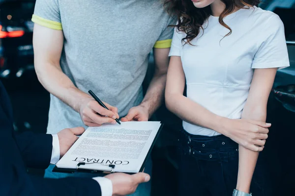 男性が女性の近くで契約書に署名しながら クリップボードを保持する車のディーラーのクロップビュー — ストック写真