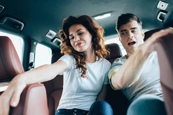 自動車のハンサムな男性の近くに座っている魅力的で巻き毛の女性の選択的焦点 — ストック写真