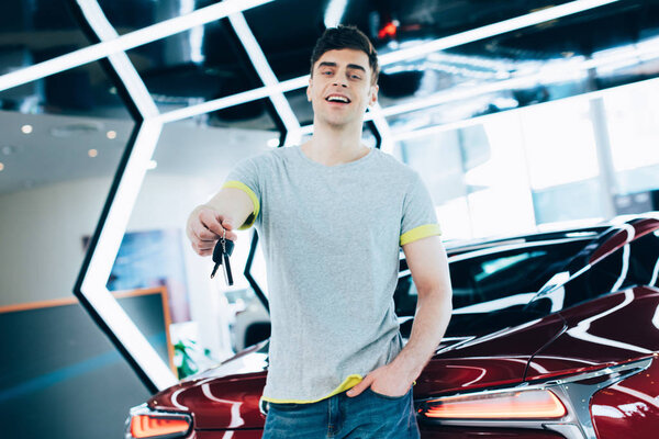 happy man standing with hand in pocket and holding keys near red car 