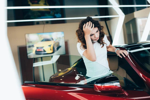 selective focus of exhausted woman standing new car in car showroom