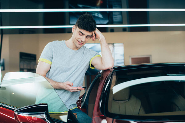 selective focus of smiling man using smartphone while standing near car 