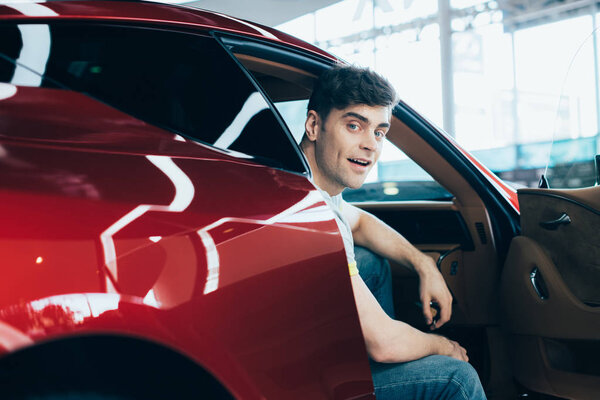 Избирательный фокус: красивый мужчина сидит в новой машине и смотрит в камеру
