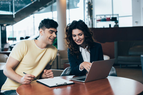 улыбающийся клиент и автомобильный дилер, сидящий за столом в автосалоне
