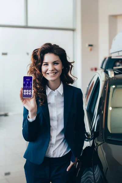 Uśmiechnięta Businesswoman Pokazując Smartfon Pulsem Tętna Ekranie Trzymając Rękę Kieszeni — Zdjęcie stockowe