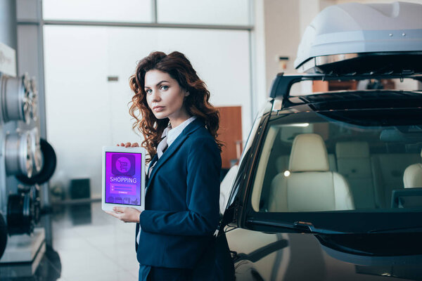 confident businesswoman holding digital tablet with shopping app on screen and looking at camera