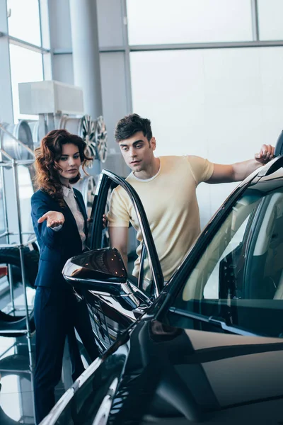 有吸引力的汽车经销商和英俊的男人站在新车附近的选择性焦点 — 图库照片
