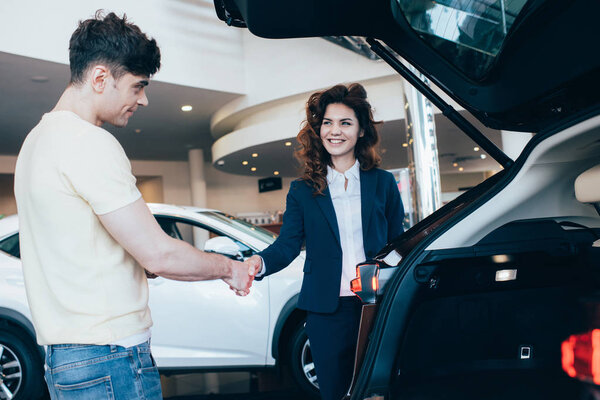 cheerful car dealer and customer shaking hands in car showroom 