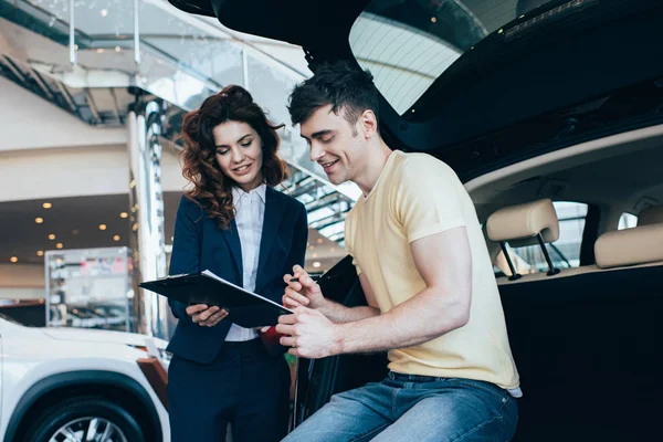 Cliente Sonriente Concesionario Coches Sujetando Portapapeles Mientras Está Pie Cerca — Foto de Stock