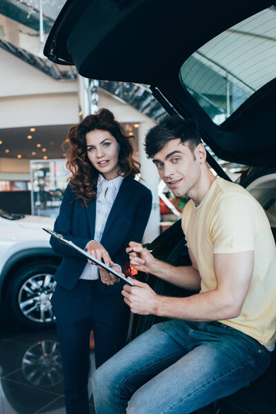 selective focus of happy man holding clipboard and car dealer standing near car