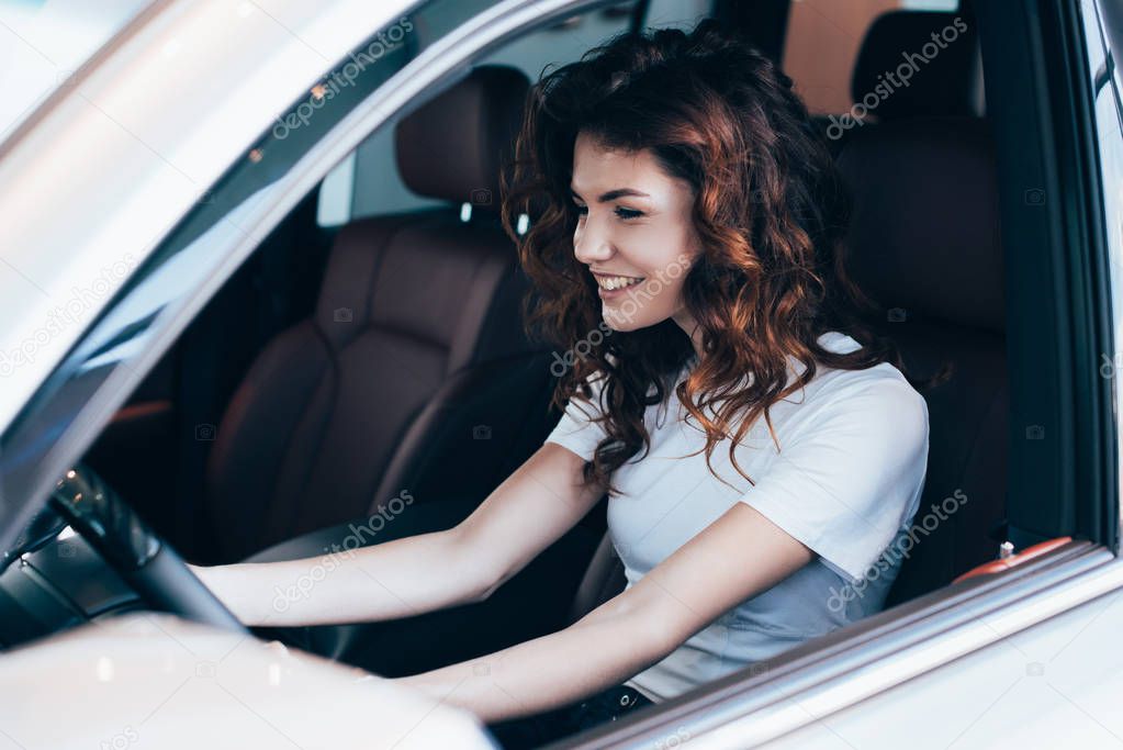 selective focus of cheerful curly woman sitting in automobile 