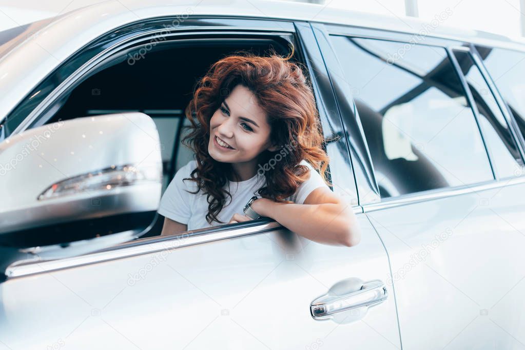 selective focus of cheerful curly woman sitting and smiling in automobile 