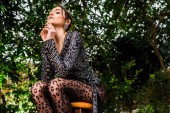 Low angle view of sexy pensive woman in black pantyhose sitting on chair in botanical garden