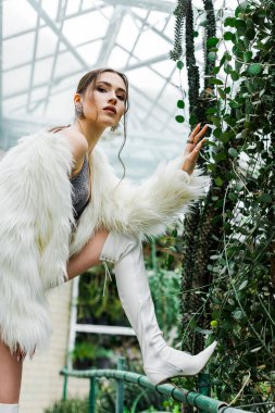 Orangery içinde yeşil yeşillik dokunmadan faux kürk paltolu kendine güvenen seksi kız