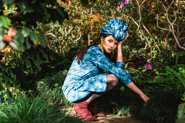 Sad pensive woman in blue dress and turban sitting in botanical garden