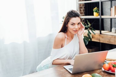 Mutfakta masada laptop kullanarak çekici genç kadın